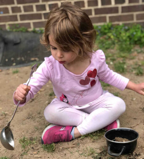 A-little-girl-plays-in-the-dirt-with-mud-kitchens-tools_optimized A young girl plays with a ladle and pot in the dirt.