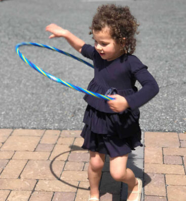 A-young-girl-hula-hooping-outside_optimized A young girl in a blue dress hula hoops.